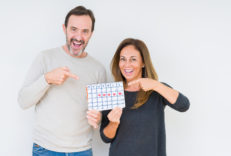 Middle age couple holding month calendar over isolated background very happy pointing with hand and finger