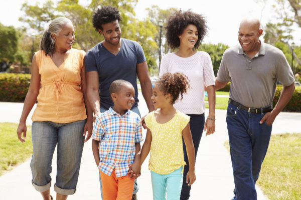 a multi-generational black family walking along a sidewalk, smiling in the sunshine