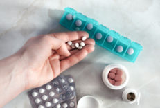 A person holding medication in their hand which is surrounded by pill bottles and a pill organizer.