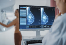 A women getting a mammogram in the background with a healthcare provider looking at her ultrasound results