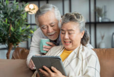 old asian senior couple sit relax happiness on sofa hand use tab